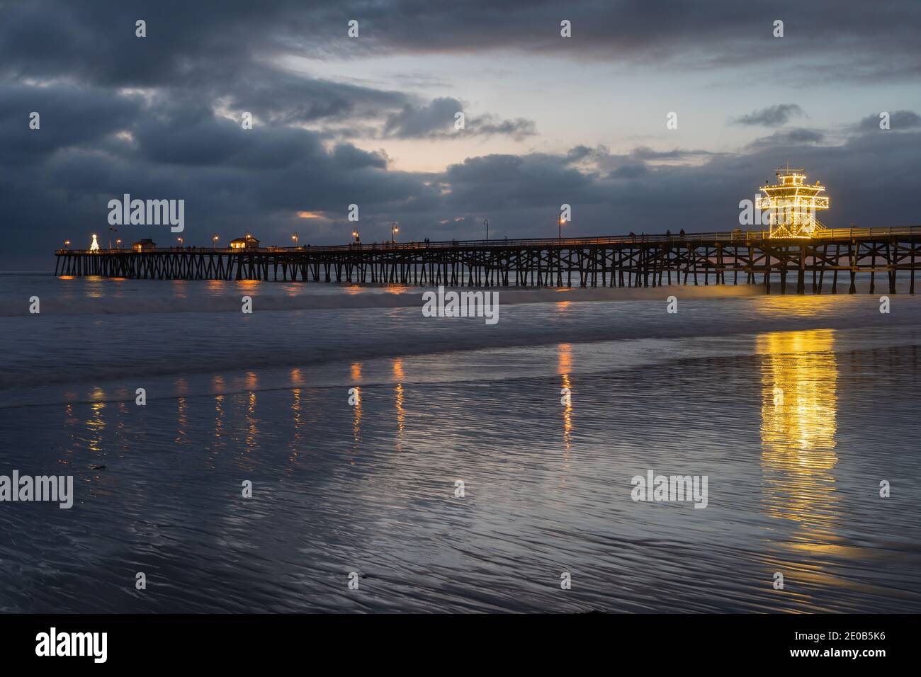 Un quai de l'océan aux lumières vives, dans une soirée froide de décembre, projette des réflexions sur les eaux douces de la plage en contrebas. Banque D'Images