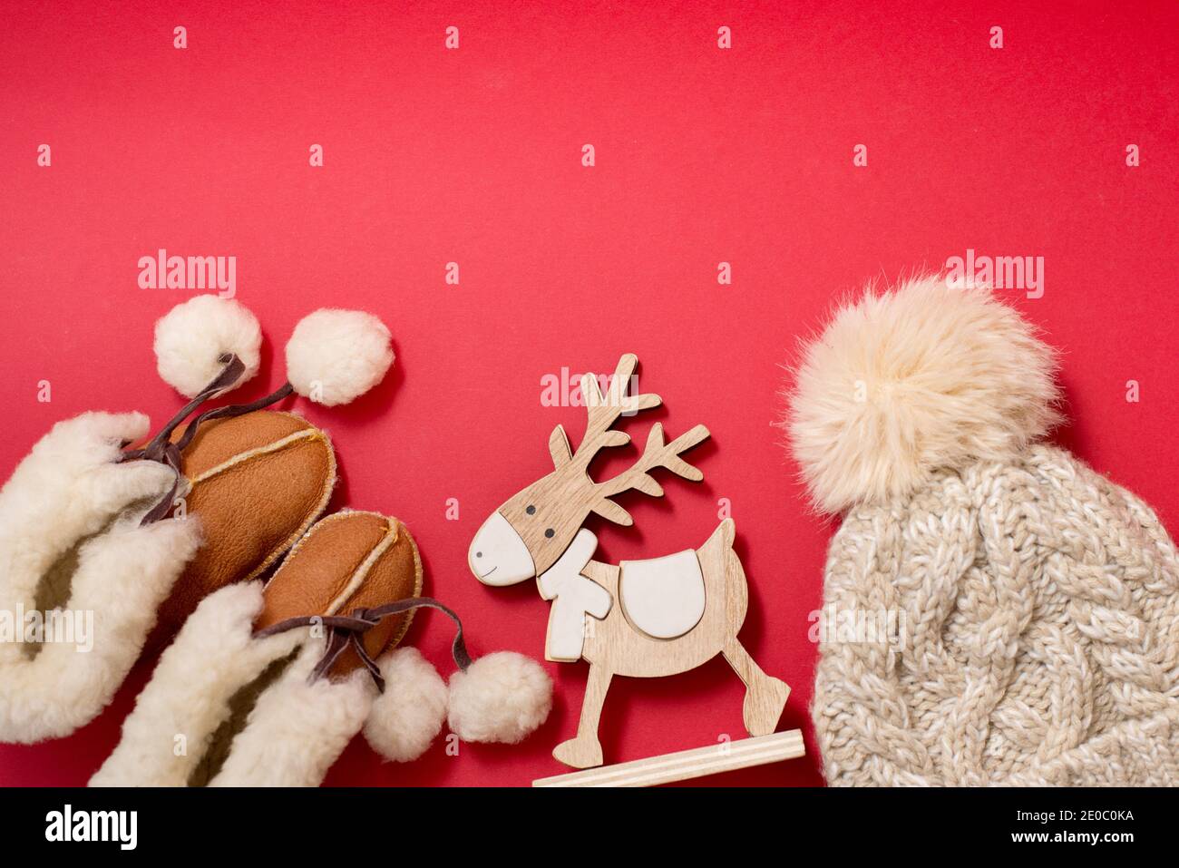 Bébé vêtements d'hiver chaussons et chapeau sur fond rouge avec cerf en bois jouet, espace de copie Banque D'Images