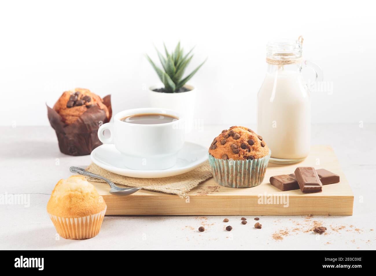 Une variété de muffins avec une tasse de chocolat au lait sur une planche de bois sur fond blanc. Banque D'Images