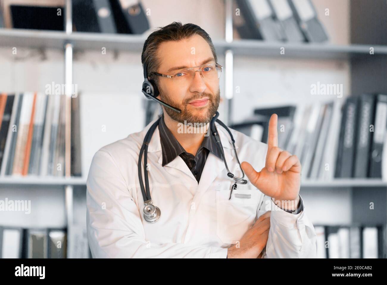 Un médecin avec micro-casque donne des conseils en ligne. Il écoute attentivement et attire l'attention sur le patient par des gestes. Banque D'Images