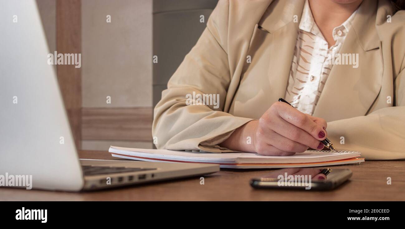 Une jeune femme d'affaires écrit des notes dans un ordinateur portable pendant qu'elle prépare des tâches hebdomadaires à l'aide d'appareils numériques dans un café. Fille Boss concept 2021. Banque D'Images
