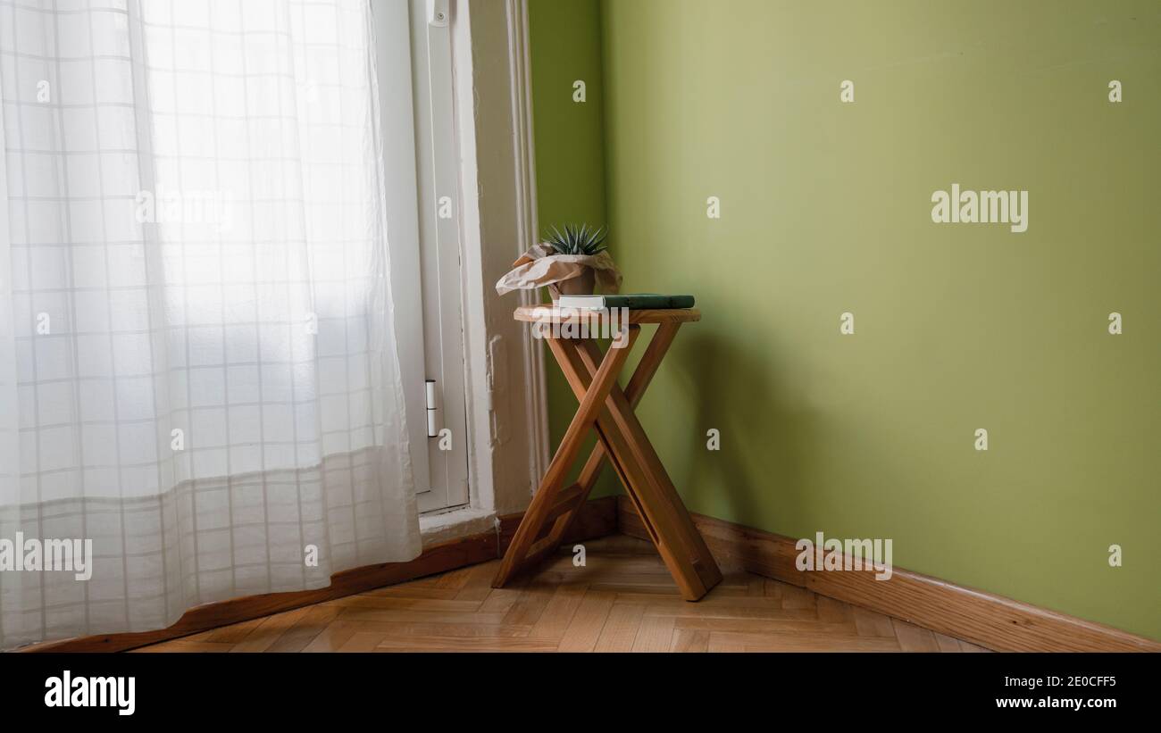 Livre et cactus sur un banc en bois dans le coin d'une chambre à côté de la fenêtre avec rideau blanc à la maison Banque D'Images