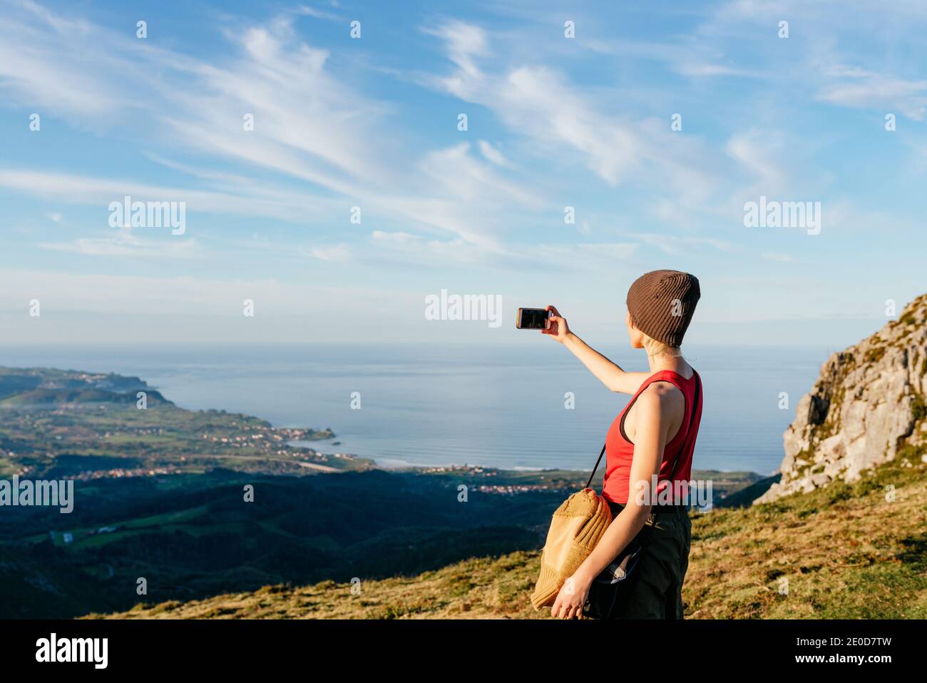 Vue latérale de l'aventurier féminin debout sur la colline dans les hauts plateaux et prendre des photos de la vallée et de la mer au coucher du soleil pendant déplacement Banque D'Images