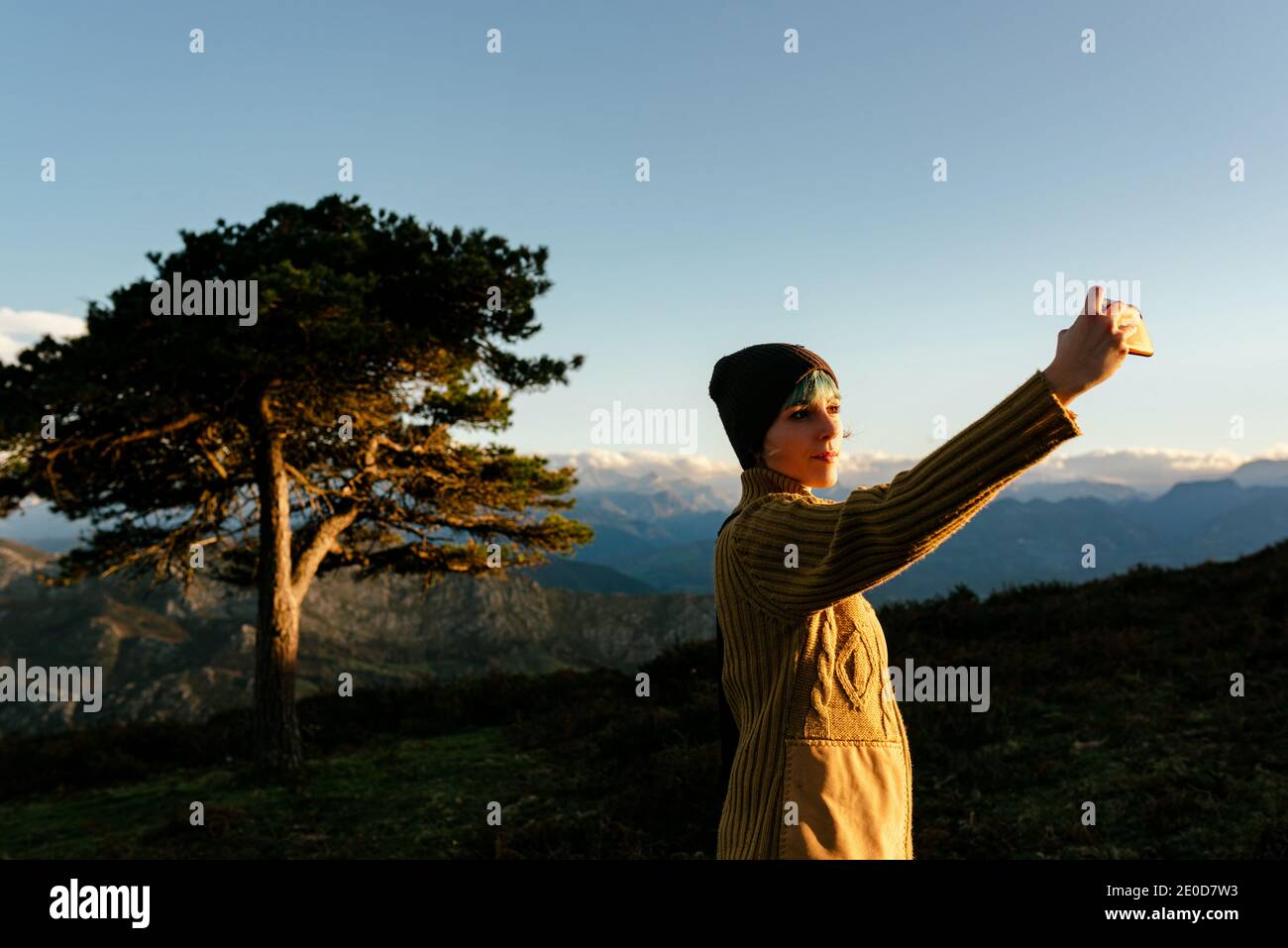Vue latérale de l'aventurier féminin debout sur la colline dans les hauts plateaux et prendre des photos de la vallée et de la mer au coucher du soleil pendant déplacement Banque D'Images