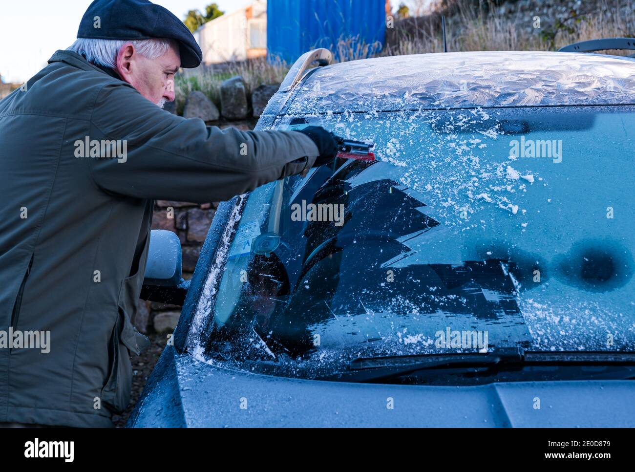 Homme senior raclant la glace du pare-brise de voiture en hiver avec des motifs de gel sur le toit de voiture, Écosse, Royaume-Uni Banque D'Images
