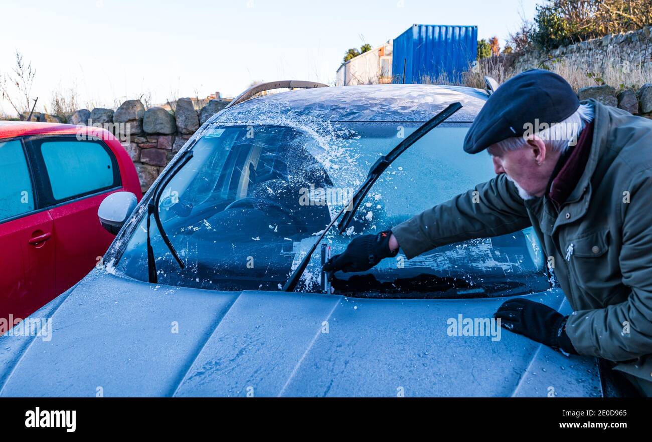 Homme senior raclant la glace du pare-brise de voiture en hiver avec des motifs de gel sur le toit de voiture, Écosse, Royaume-Uni Banque D'Images