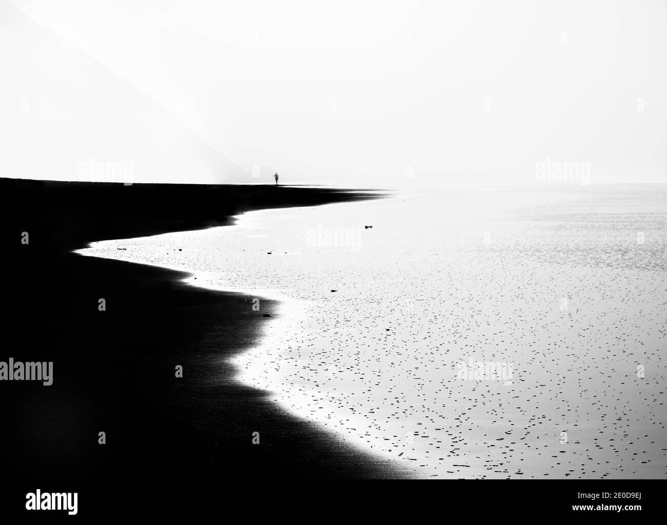 Photo noir et blanc à contraste élevé prise sur la plage de Bayas, Asturies. Au coucher du soleil avec une figure humaine dans l'arrière-plan tout en marchant sur le b Banque D'Images