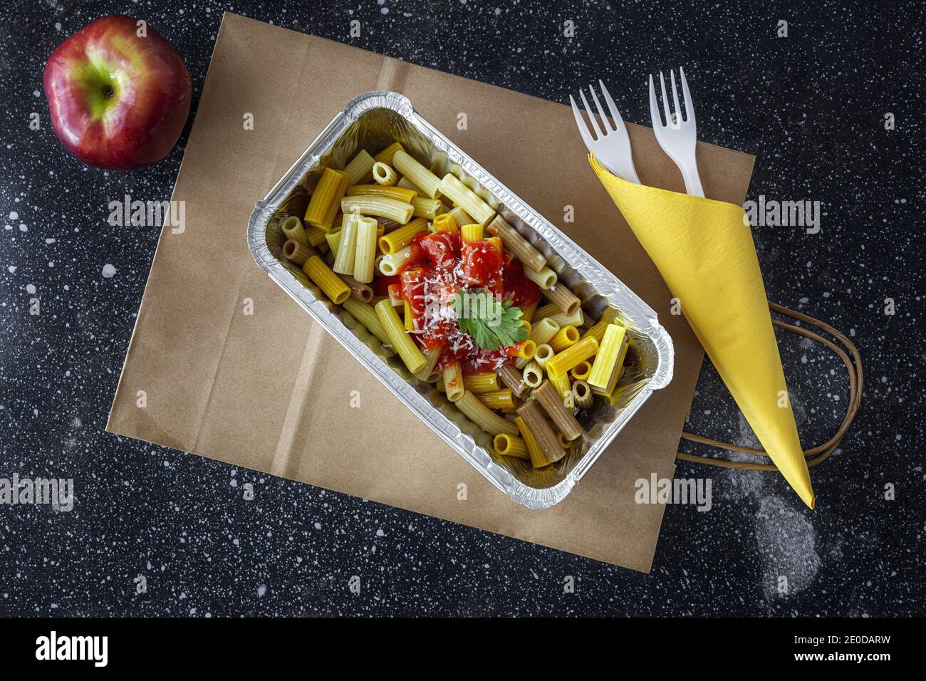 Du dessus de délicieux macaroni au ketchup et au fromage dans un récipient pour les plats à emporter sur la table avec la pomme Banque D'Images