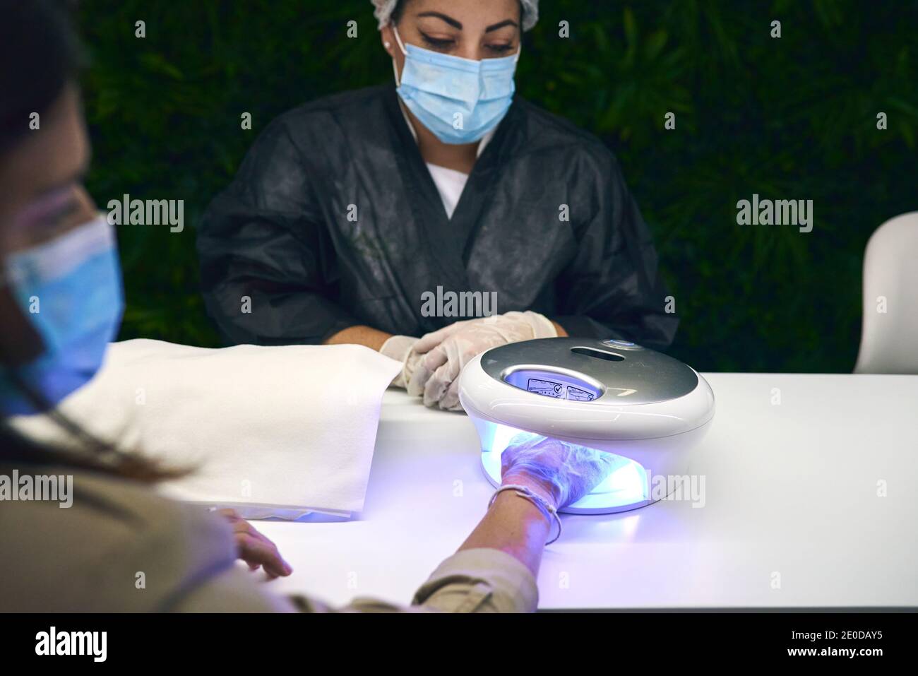 Cliente assise à table avec un artiste de l'ongle et utilisant Lampe UV moderne pour la manucure de gel dans le centre de beauté Banque D'Images
