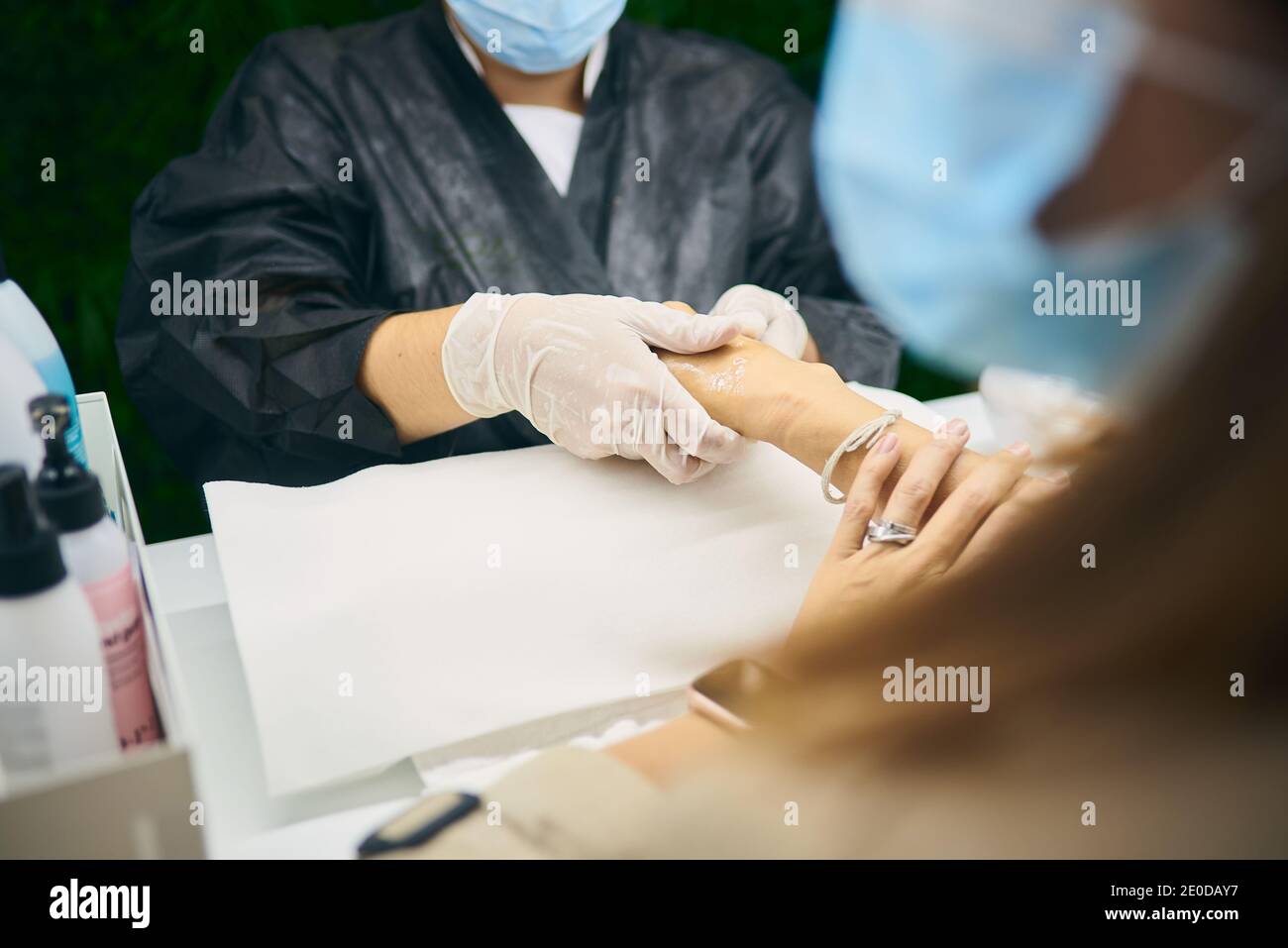 Crop anonyme ongles artiste appliquant la crème hydratante pour les mains après avoir fait manucure pour la cliente féminine dans un salon moderne pendant l'épidémie de coronavirus Banque D'Images