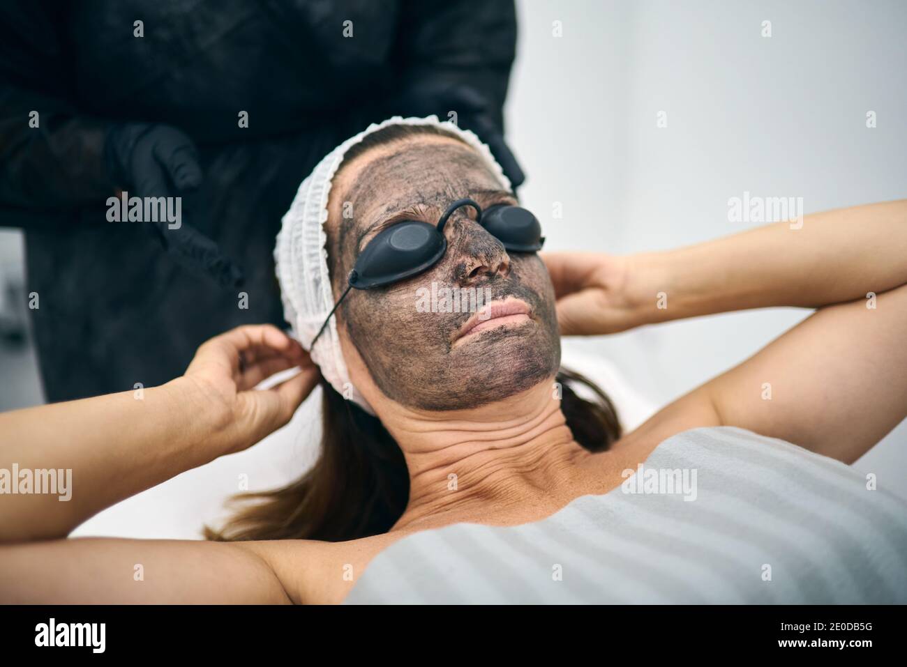 Cliente féminine avec lotion carbone sur le visage mettant sur la protection lunettes tout en se préparant au pelage au laser dans le centre de beauté moderne Banque D'Images