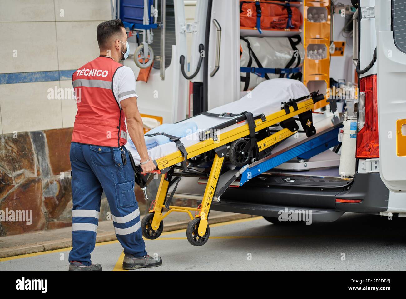 Vue latérale d'un professionnel de l'aide médicale mâle dans le masque de protection tirant civière hors de la camionnette d'ambulance garée dans la rue Banque D'Images