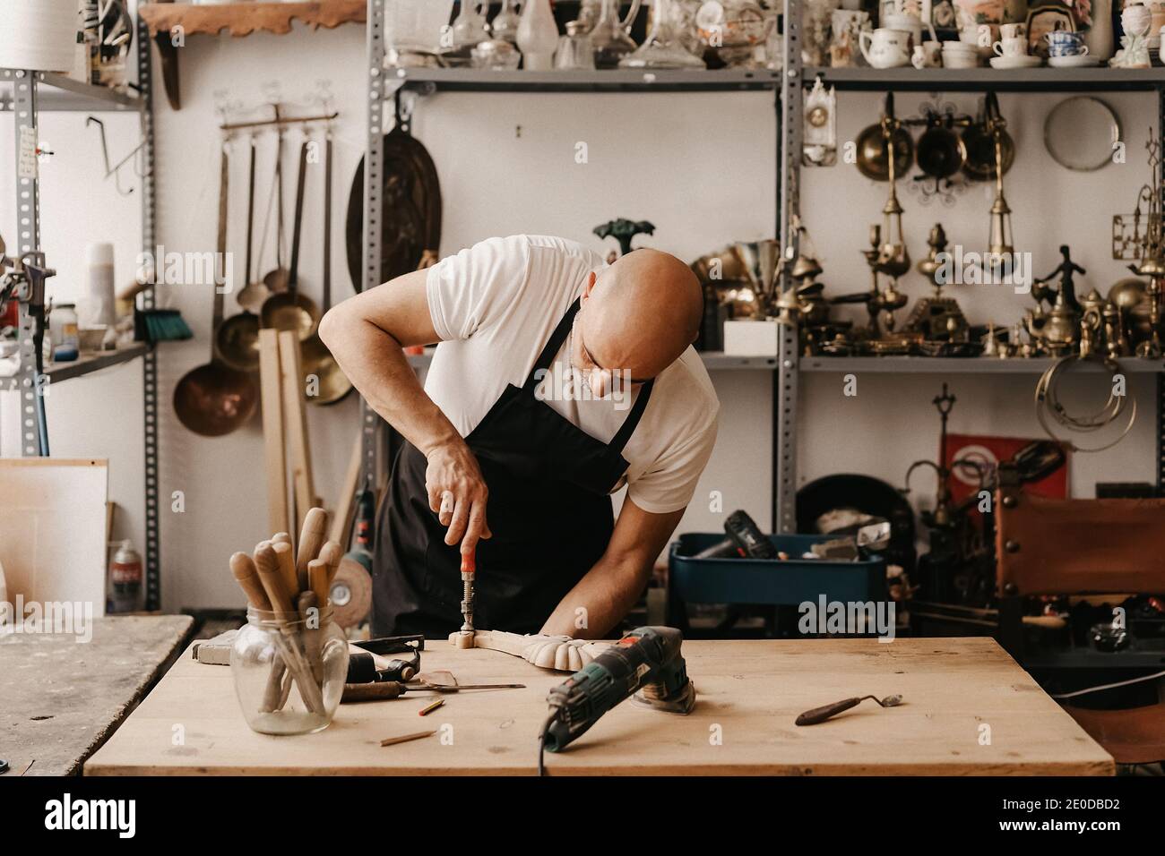 Travailleur du bois en tablier sculptant le bois avec le burin et le marteau pendant création de détails ornés dans l'atelier Banque D'Images