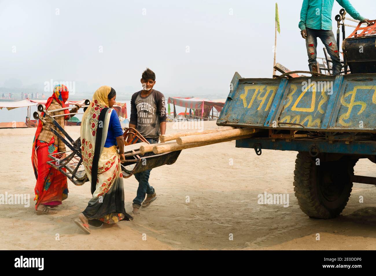 Des femmes et des hommes chargent des chaises de grande roue démantelées sur un camion d'attente lors d'une chaude journée estivale le long de la rivière Yamuna à Vrindavan, Uttar Pradesh, Inde. Banque D'Images