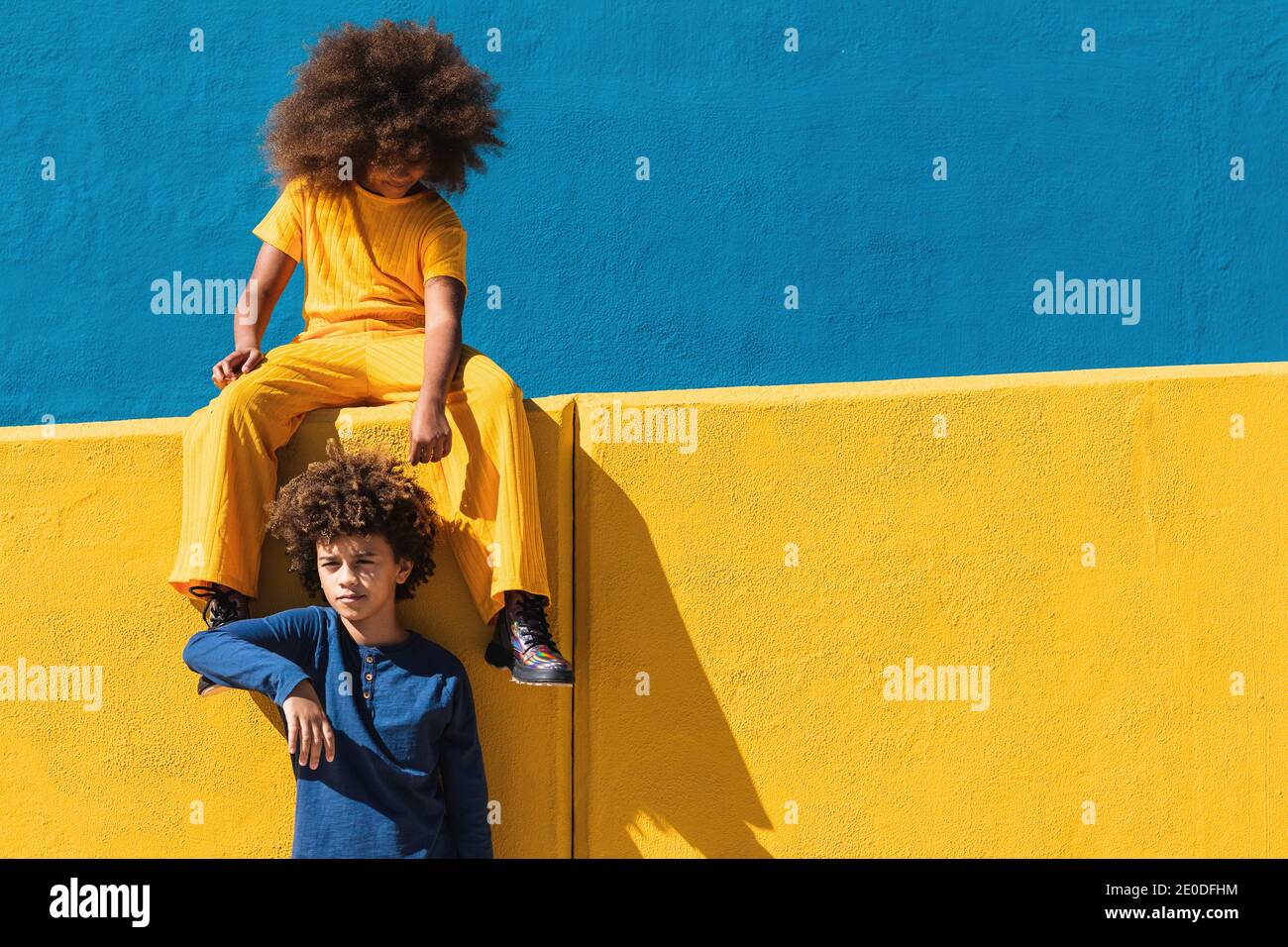 Ado afro americain fille et garcon avec le port de coiffure d afro vetements colores se reposant ensemble contre le mur bleu et jaune journee ensoleillee dans la rue Photo Stock Alamy