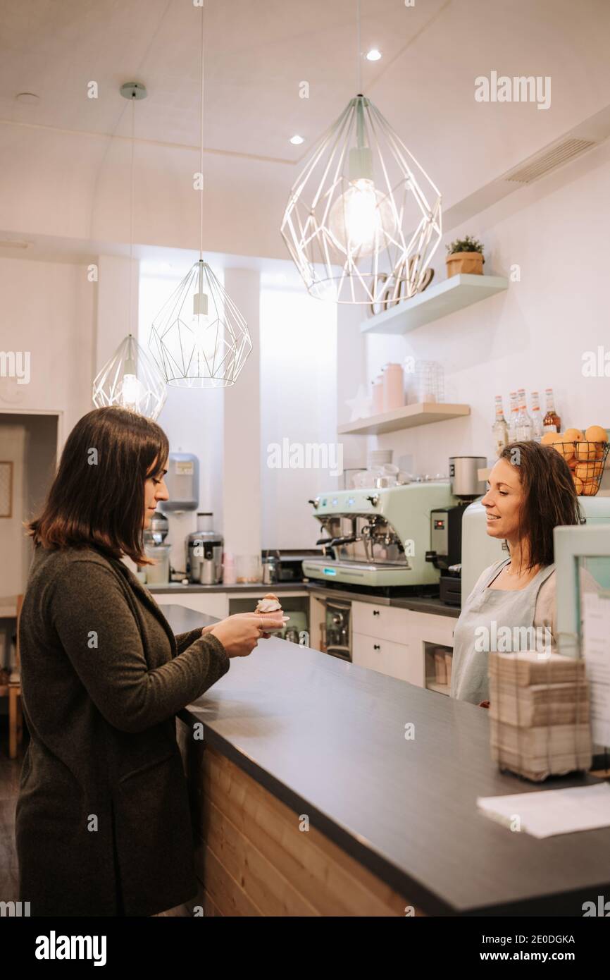 Une femme positive se tient au comptoir et sert du gâteau pour client travaillant dans un magasin de confiserie moderne Banque D'Images