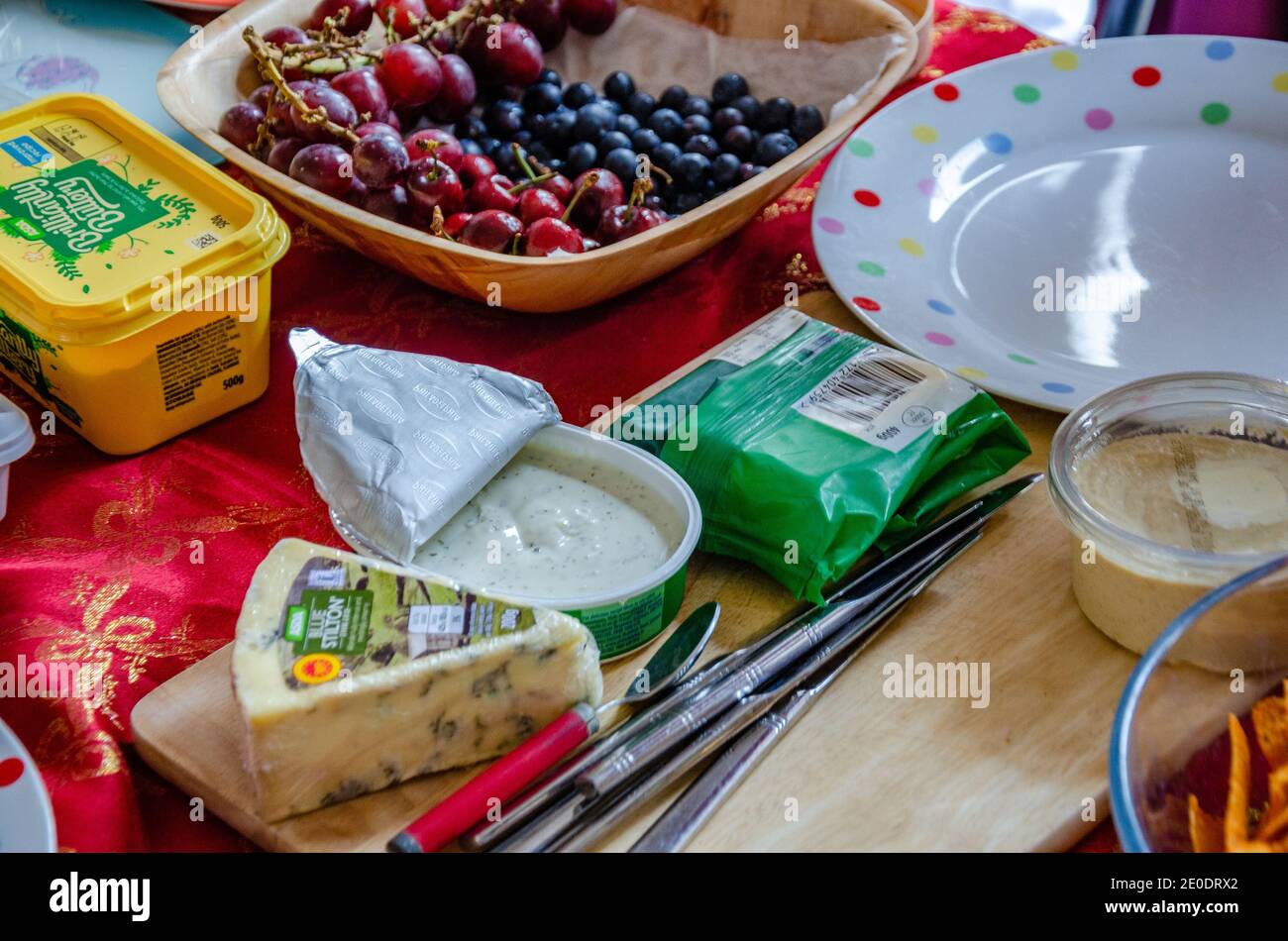 Plats disposés sur une table pour un déjeuner buffet comprenant du fromage, du beurre, un bol de fruits avec une poignée de couteaux sur une planche à découper en bois. Banque D'Images