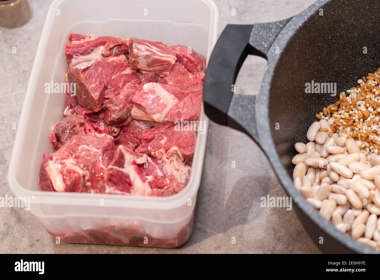 Gros plan du Hamin traditionnel juif Cholent - plat principal pour le repas Shabbat bœuf lentement cuit avec pommes de terre, haricots, grains de blé et épices dans une casserole sur une table de cuisine en marbre gris. Banque D'Images