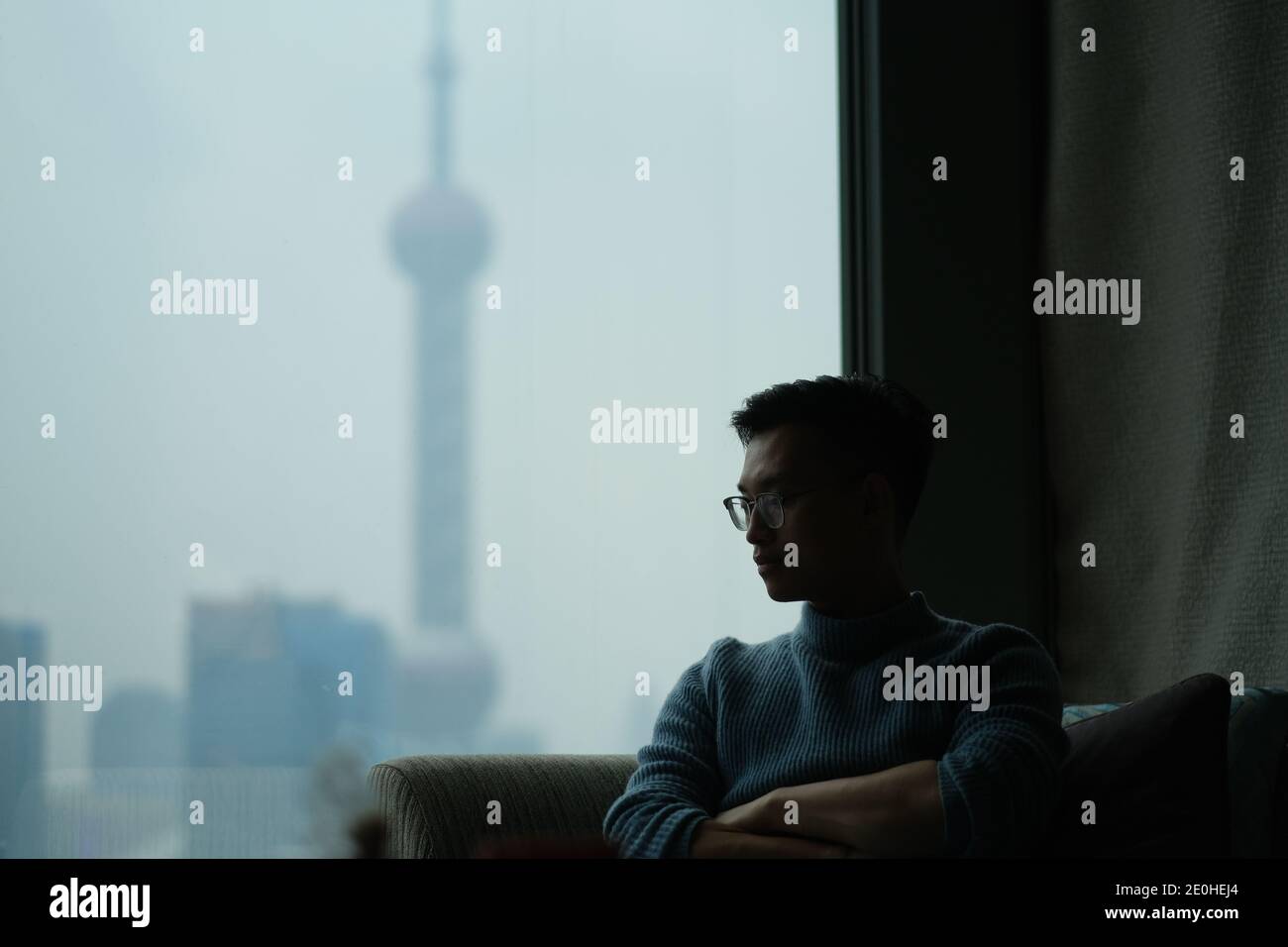 Photo d'un jeune asiatique assis près de la fenêtre perdue dans la pensée, flou moderne repère hors de la fenêtre Banque D'Images