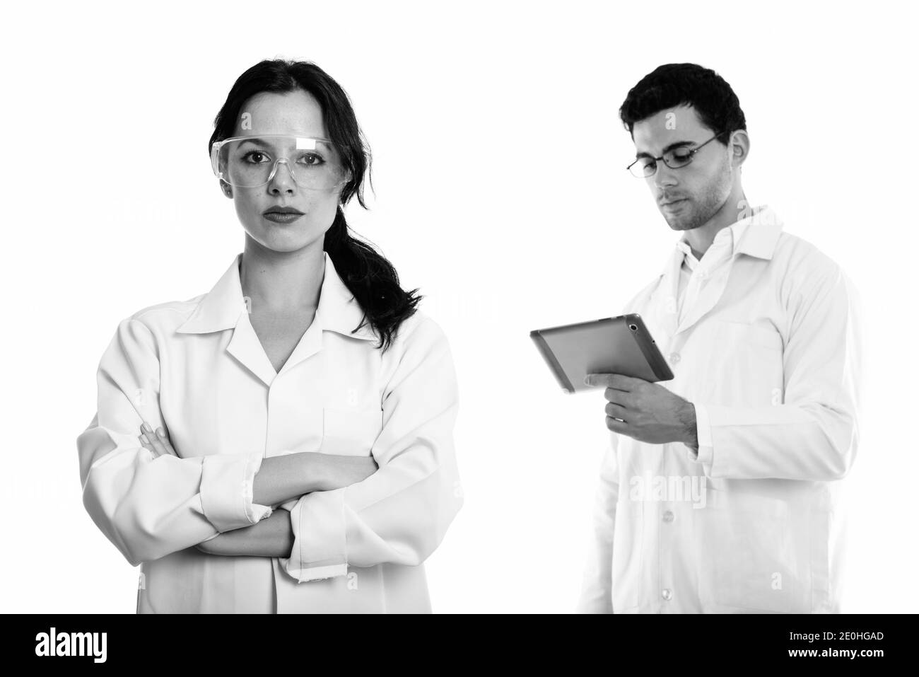 Jeune femme médecin portant des lunettes avec les bras croisés et l'homme médecin using digital tablet Banque D'Images