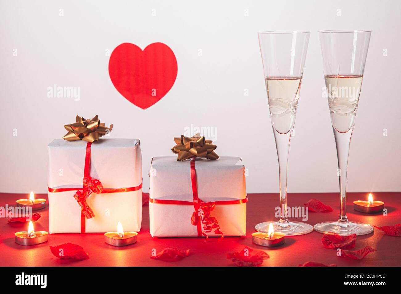 Composition de la Saint-Valentin avec deux verres de champagne, coeur, cadeaux et bougies sur fond rouge. Concept de San Valentin et d'Amour. Banque D'Images