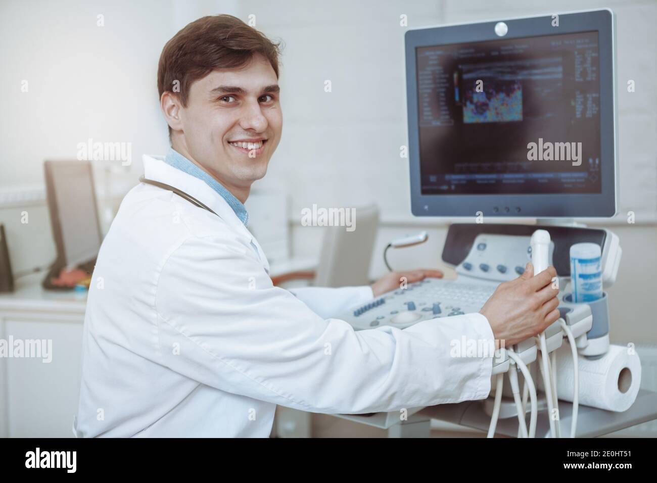 Joyeux médecin souriant à l'appareil photo, travaillant sur l'échographe dans sa clinique. Médecin expérimenté travaillant à la médecine moderne f Banque D'Images