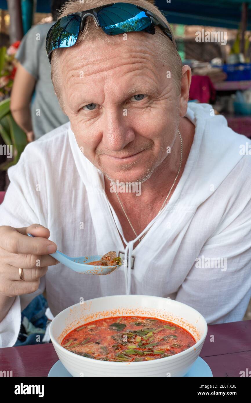 Un homme âgé adulte dans une tunique blanche mange une soupe thaï épicée  Tom Yam dans un café. Le tourisme gastronomique en Asie. Cuisine  traditionnelle épicée Photo Stock - Alamy