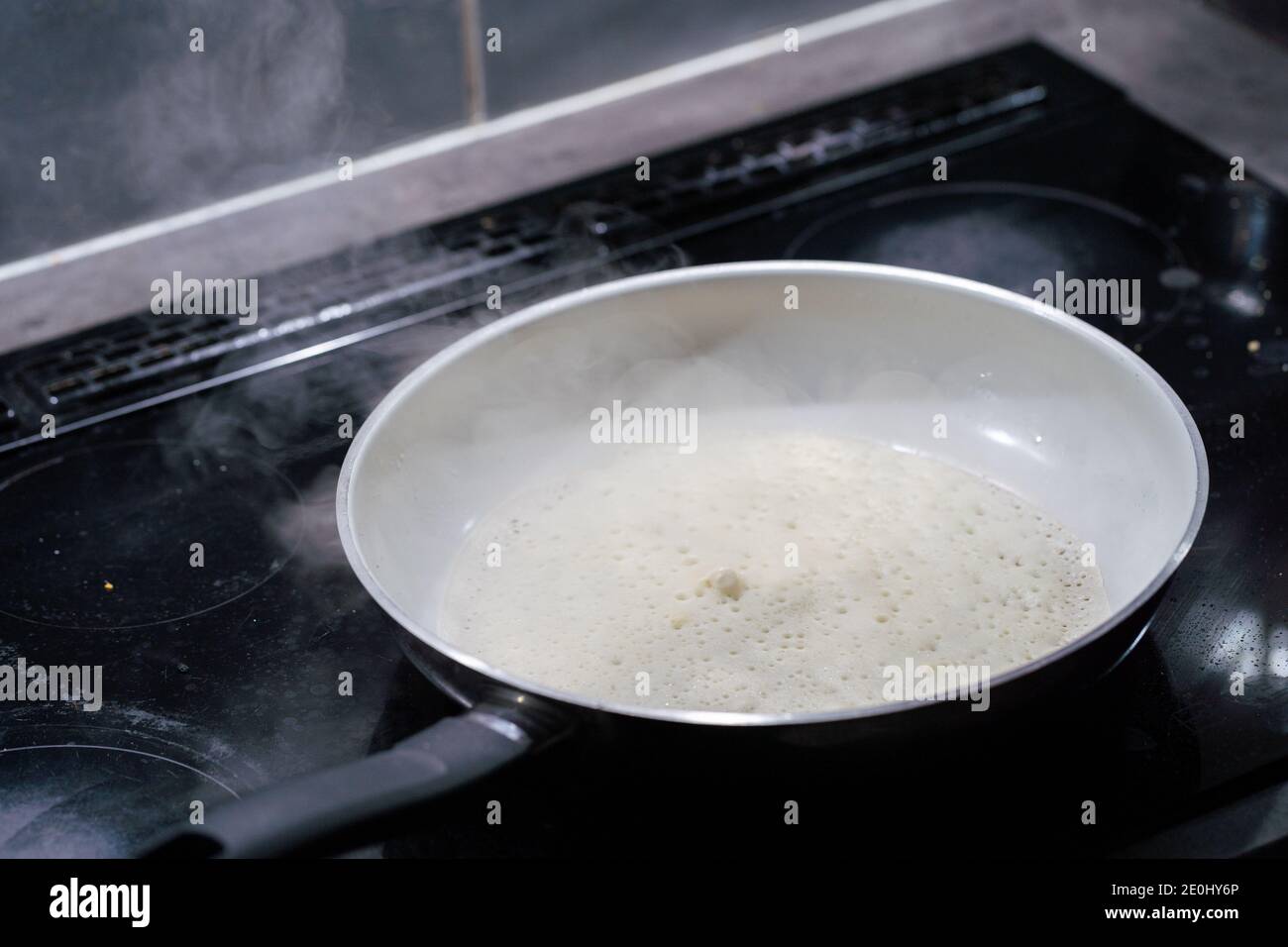 Une grande poêle repose sur la cuisinière à induction et à l'intérieur se  trouve une pâte à crêpes qui est frite. L'eau s'évapore de la cuve Photo  Stock - Alamy