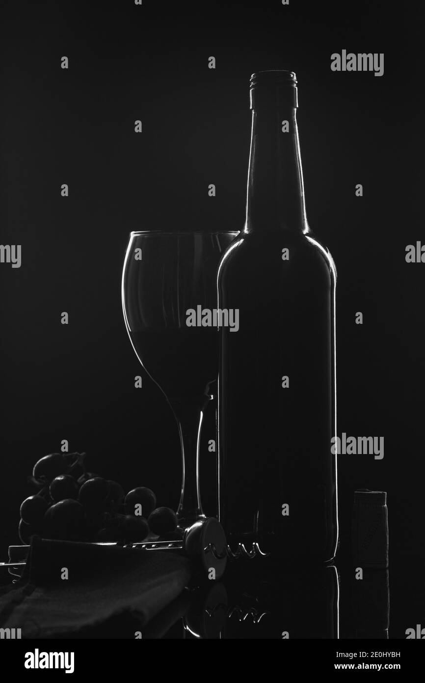 Silhouette d'une bouteille de vin, d'un verre de vin et de raisins fond noir. Banque D'Images