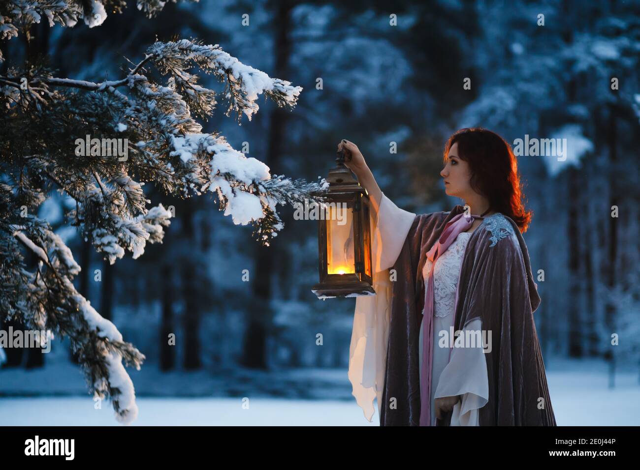 Fantaisie : la jeune femme tient une lanterne vintage éclairant le sapin couvert de neige dans la soirée. Concept cosplay médiéval de conte de fées Banque D'Images