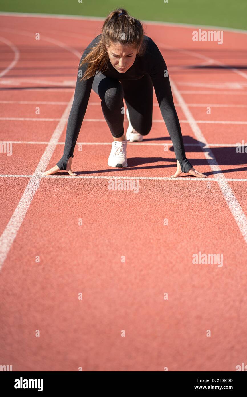 Une jeune femme pleine d'assurance sprinter sur un tapis roulant en caoutchouc stade ou sur une piste de course à pied se préparer pour commencer à courir. Banque D'Images