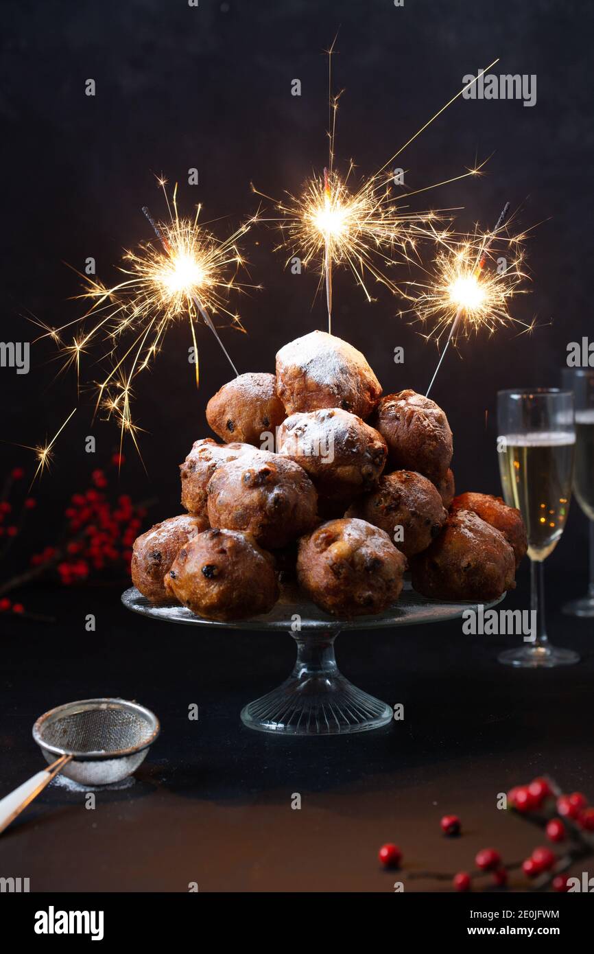 Une pile d'oliebollen hollandaise traditionnelle (traduction : boules de pâte frite) sur un support en verre avec des sparkles et deux verres de champagne Banque D'Images