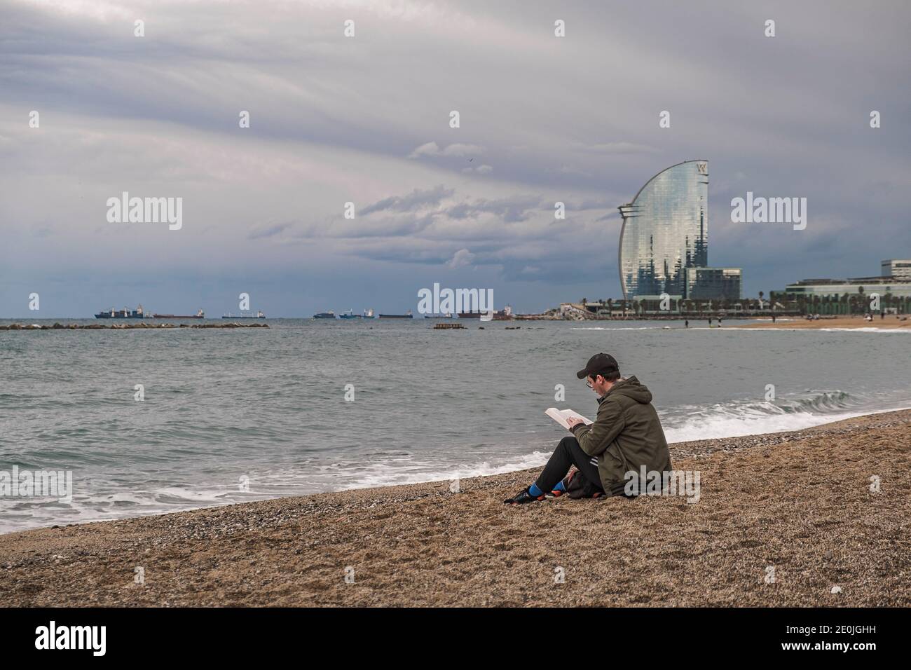 Un homme est vu assis à la plage de barceloneta tout en lisant un livre au lieu de se baigner.comme une tradition, certaines personnes sont allés à la plage pour prendre leur première baignade de l'année, une activité que les clubs de sport ont été forcés d'annuler cette année en raison de la Covid19. Barcelone prévoit de nouvelles mesures restrictives prochainement en raison de l'augmentation des infections à Covid19. Banque D'Images