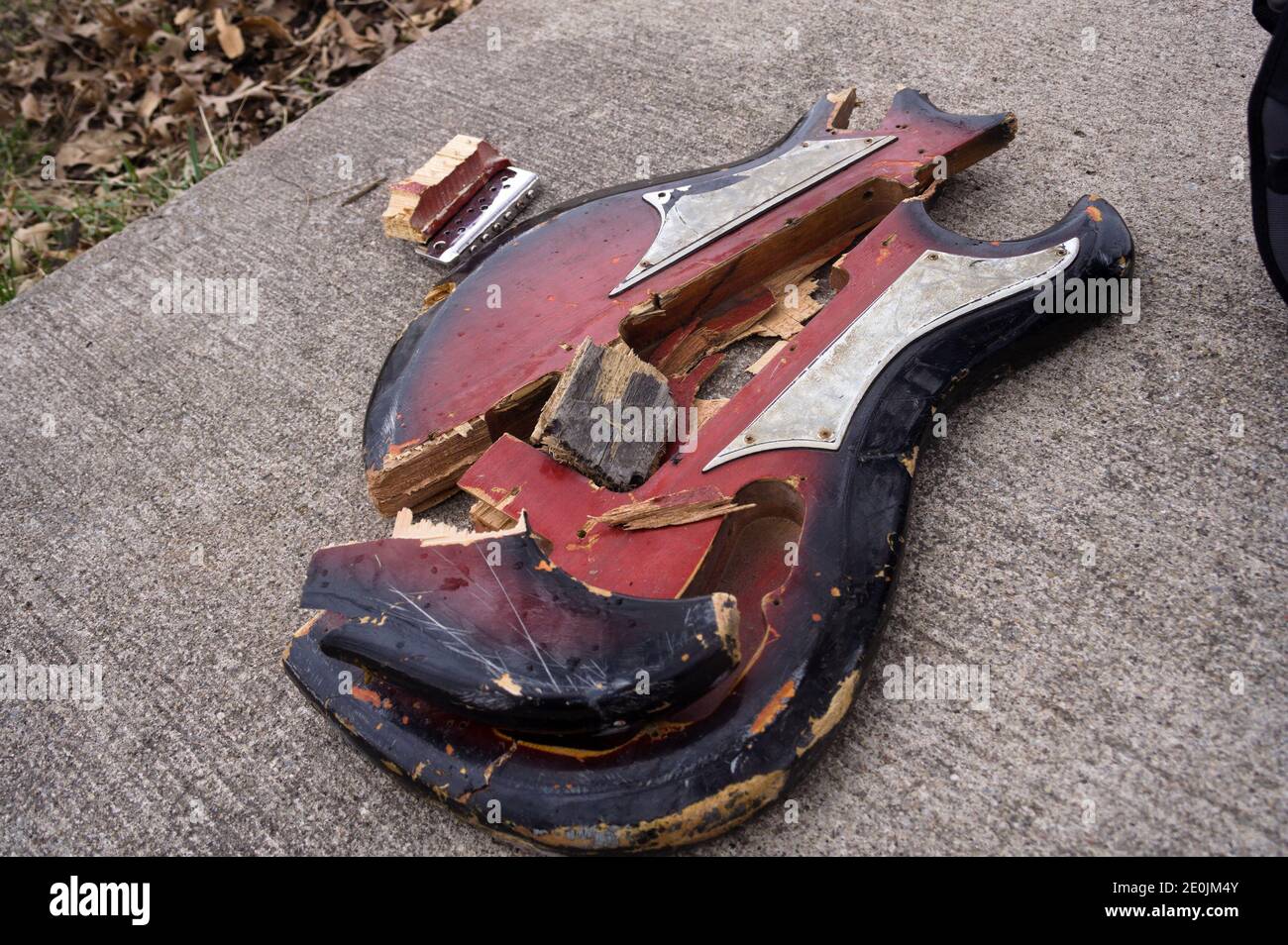 Les morceaux d'une guitare rouge brisée sont ensemble sur du béton brut. Banque D'Images