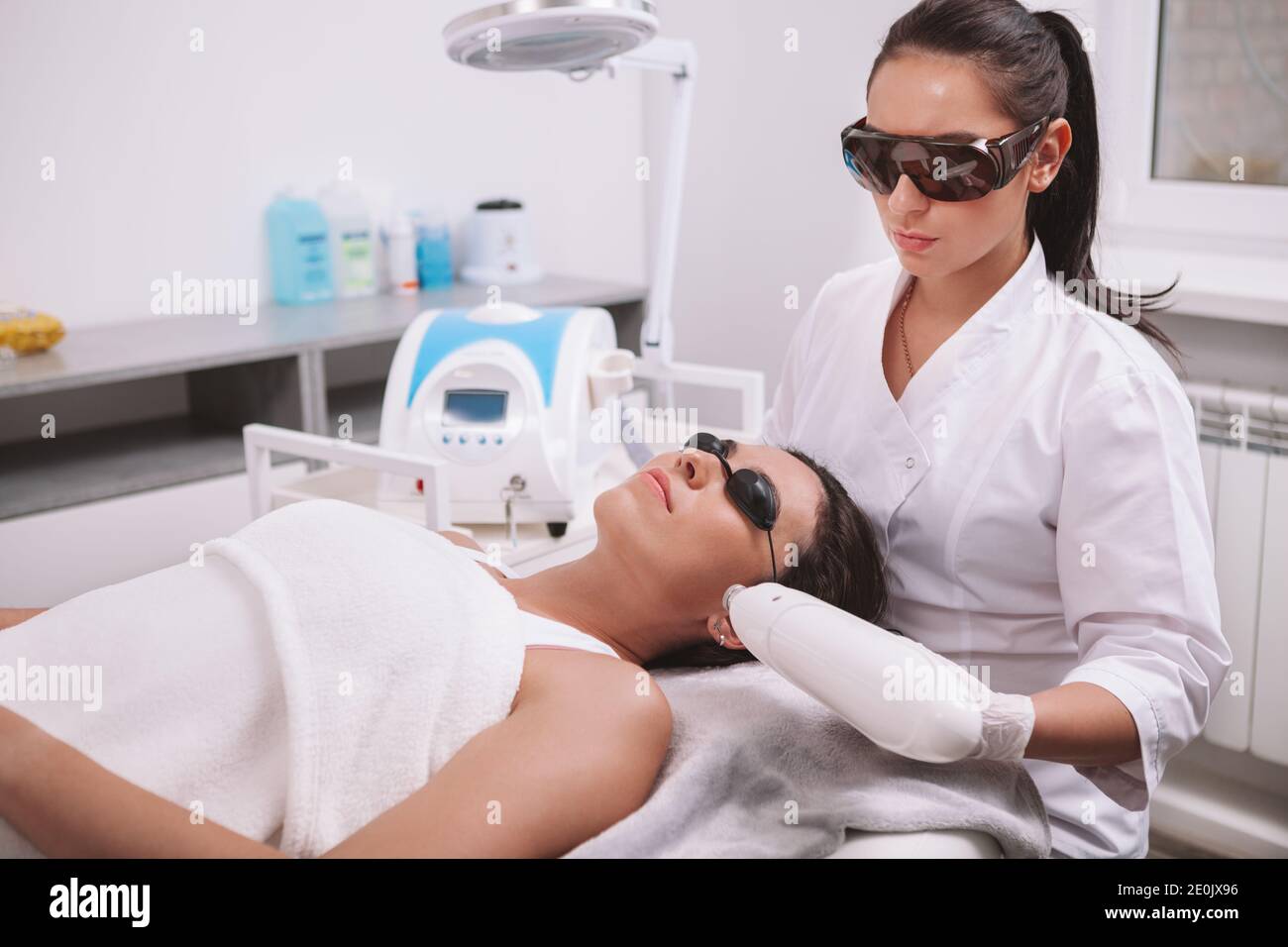 Cosmetologiste professionnel utilisant la machine d'épilation laser,  travaillant avec la cliente féminine. Jeune femme qui reçoit un traitement  laser de soin de la peau à la clinique de beauté Photo Stock -