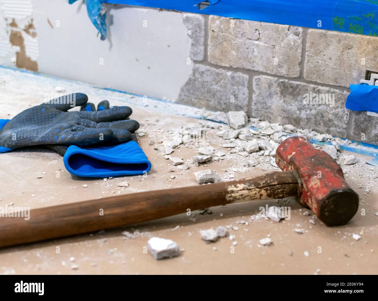 Une paire de gants usagés et un marteau en traîneau sont placés à côté d'une pile de gravats lors de la démolition d'un dosseret. Banque D'Images