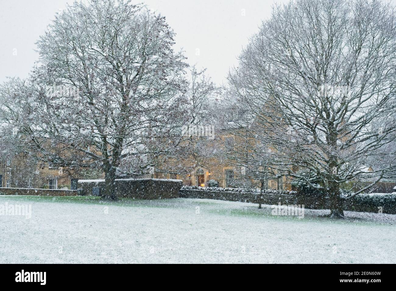 Maison en pierre Cotswold et arbres dans la neige à noël. Shipton sous Wychwood, Cotswolds, Oxfordshire, Angleterre Banque D'Images