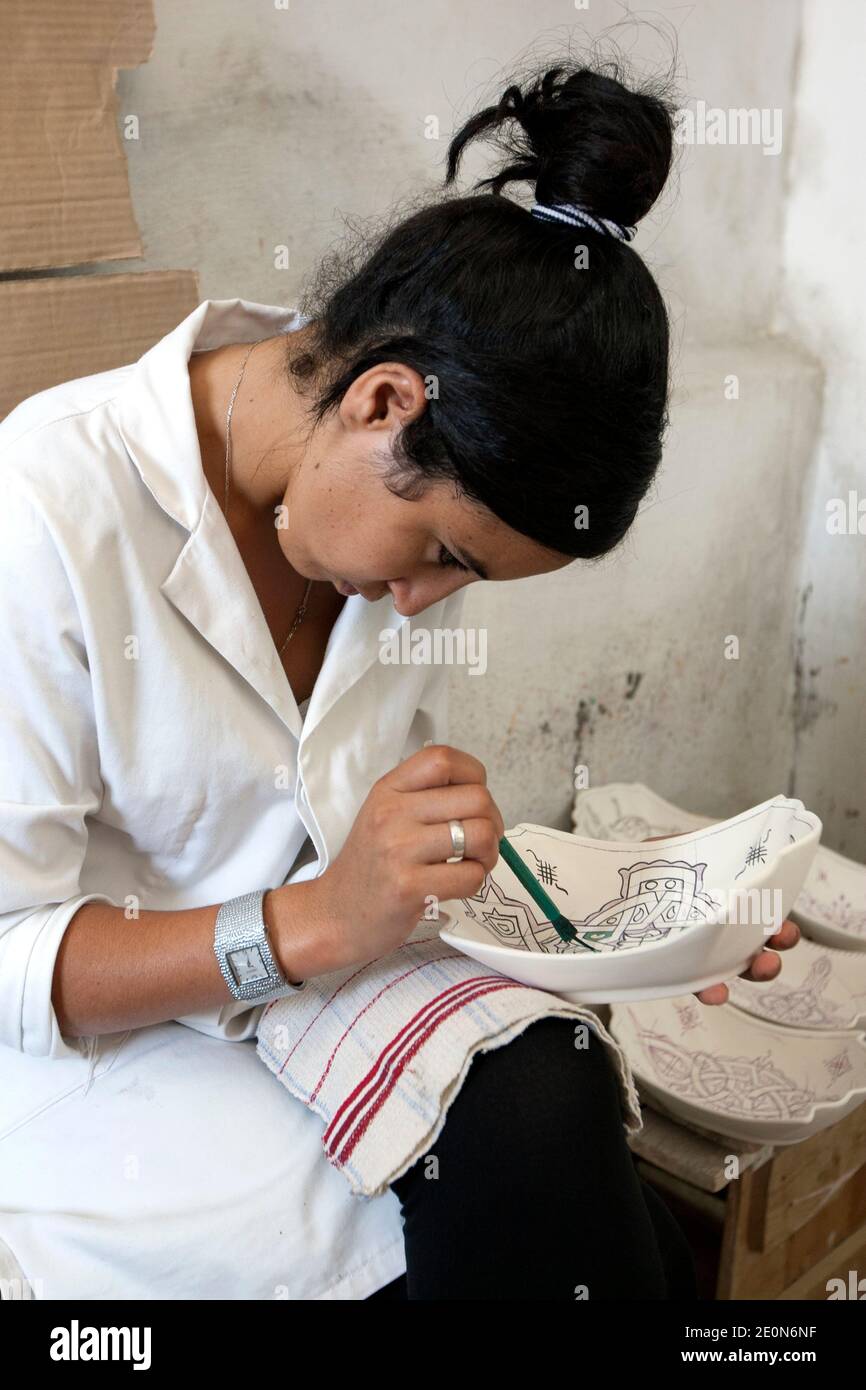 Un ouvrier commence le processus de peinture de dessins sur un bol en argile à l'usine Art Naji à Fès, au Maroc. Banque D'Images