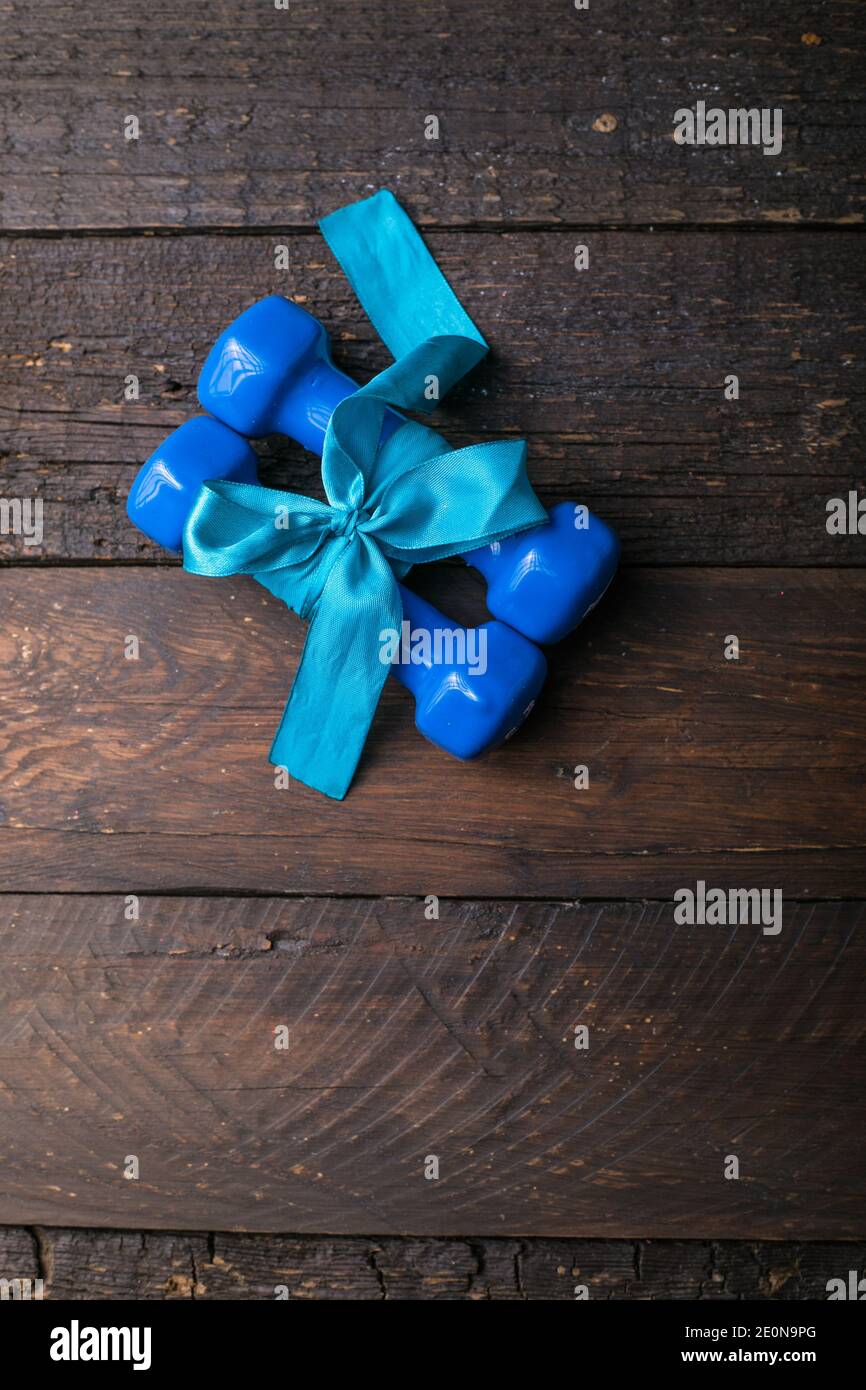 deux haltères bleues avec noeud cadeau et étiquette en papier vierge, coeur sur planches en bois, concept vacances sport Banque D'Images