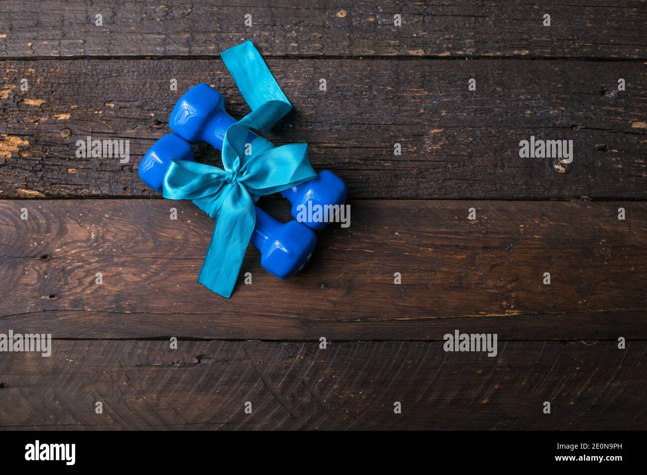 deux haltères bleues avec noeud cadeau et étiquette en papier vierge, coeur sur planches en bois, concept vacances sport Banque D'Images