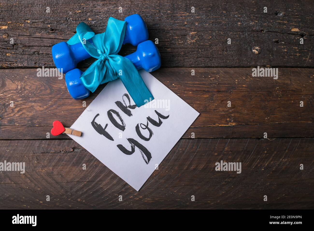 deux haltères bleues avec noeud cadeau et étiquette en papier vierge, coeur sur planches en bois, concept vacances sport Banque D'Images