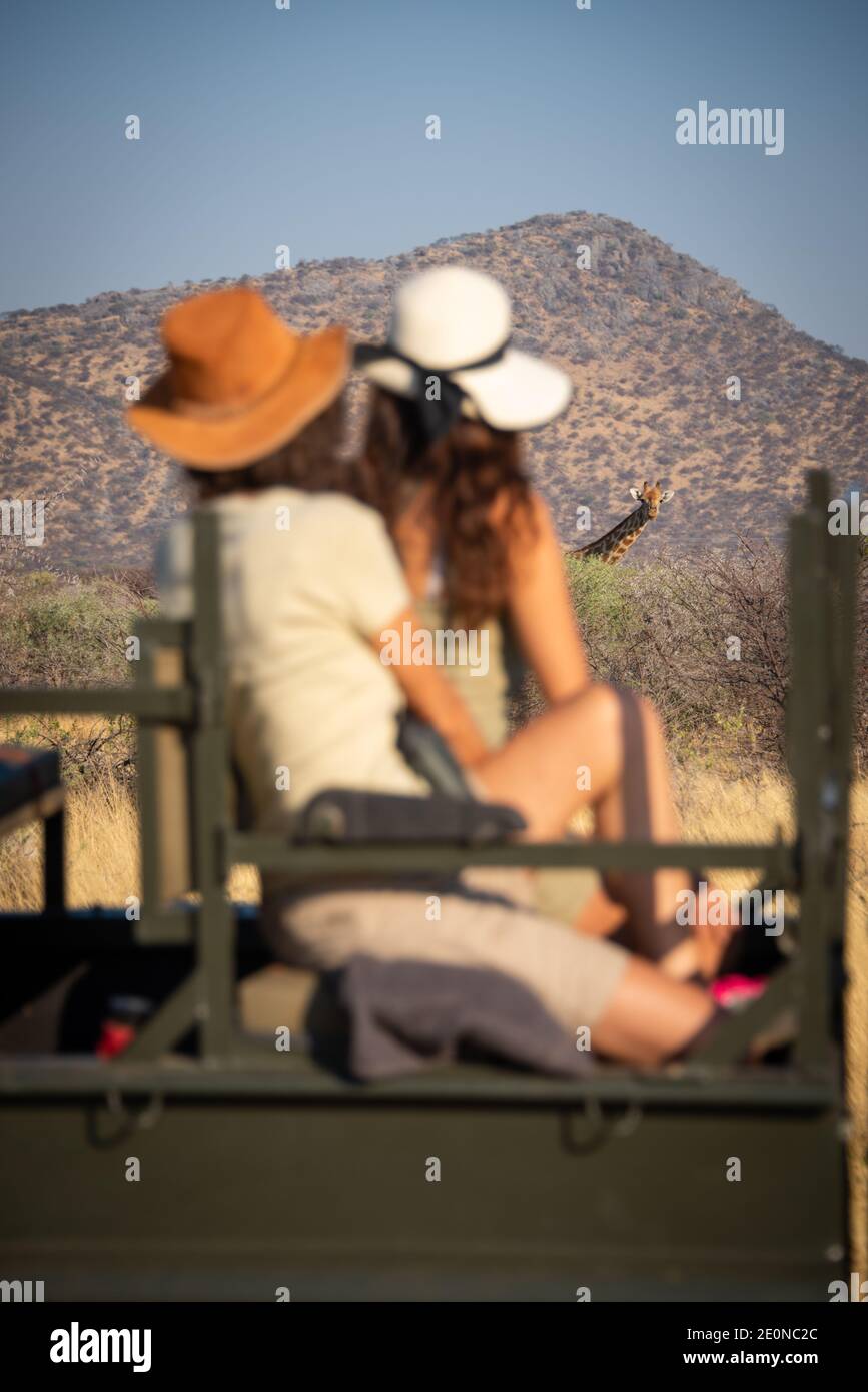 Giraffe regarde deux femmes assises en jeep Banque D'Images