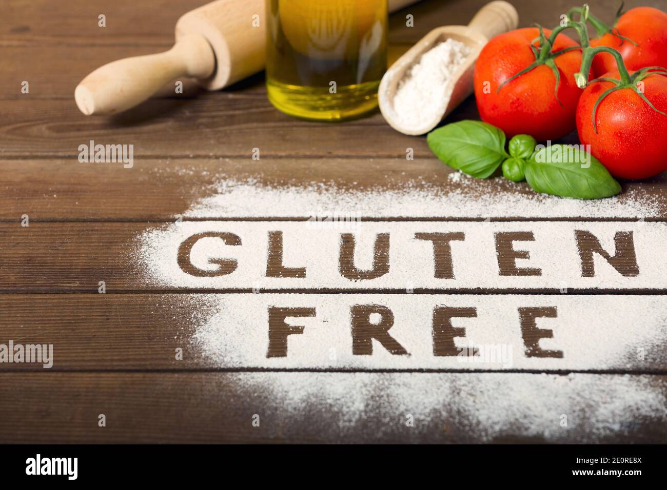 un mot « sans gluten » fait de farine sur fond de bois rustique, avec tomate, basilic, bouteille d'huile, rollpin et cuillère de farine. cousine italienne. Banque D'Images