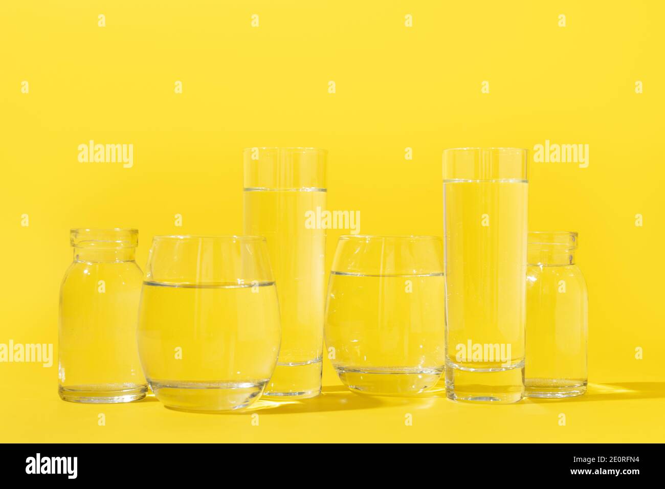 Verres avec de l'eau propre de différentes formes sur jaune. Concept des avantages de l'eau propre et douce. Équilibre de l'eau. Tarif journalier. Couleur tendance Ilumina Banque D'Images