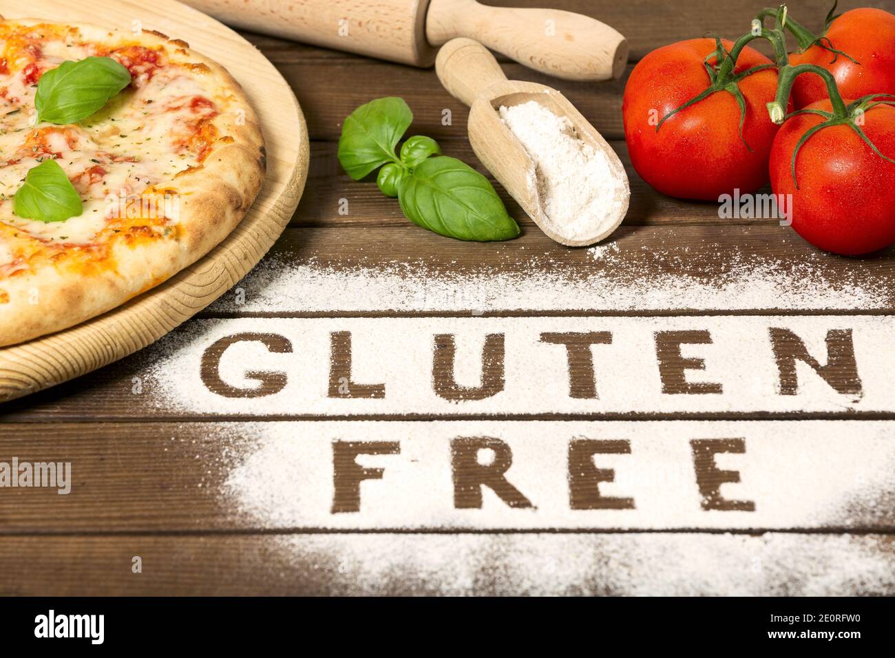 Une pizza sans gluten sur fond de bois rustique, avec le mot « sans gluten » fait de farine, de tomate, de basilic, d'une cuillère de farine. Gros plan Banque D'Images