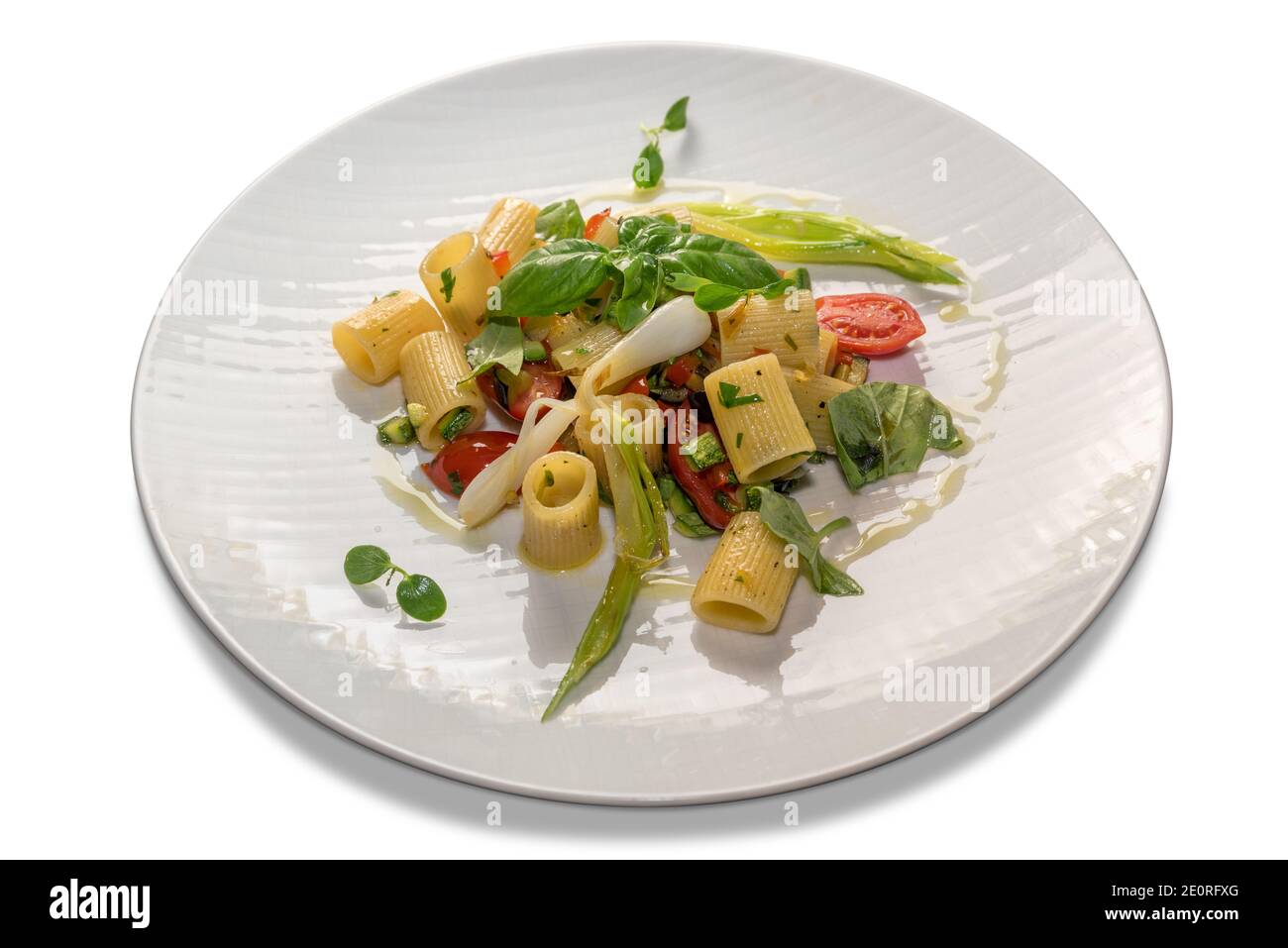 pacheri à moitié rayé avec tomates, basilic et oignon de printemps. Pâtes macaroni italien cuit assaisonné dans une plaque blanche isolée sur fond blanc Banque D'Images