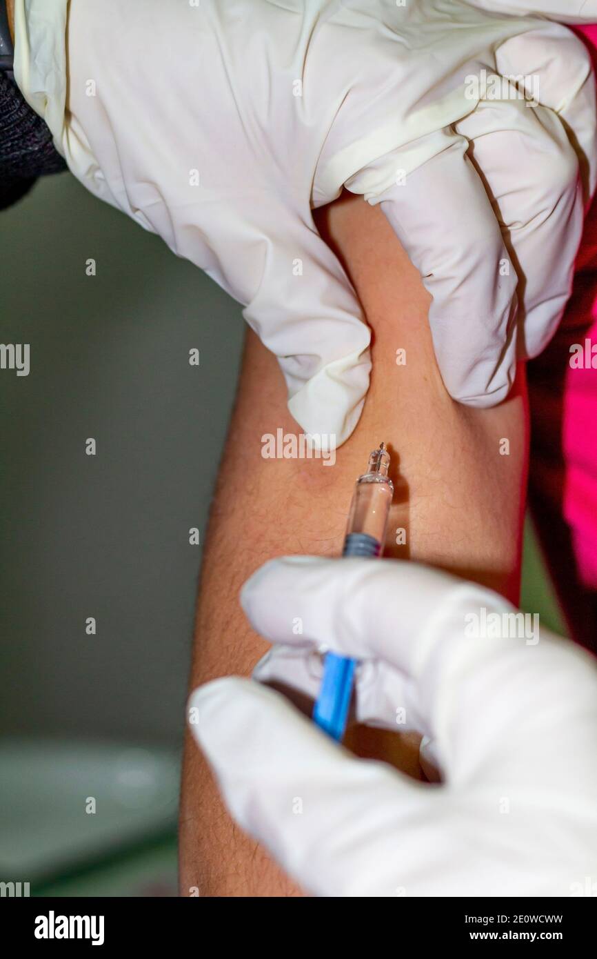 Covid-19: La main de l'infirmière en blanc injecte un vaccin contre Covid-19 (SRAS-COV-2) dans le bras d'un enfant. Banque D'Images