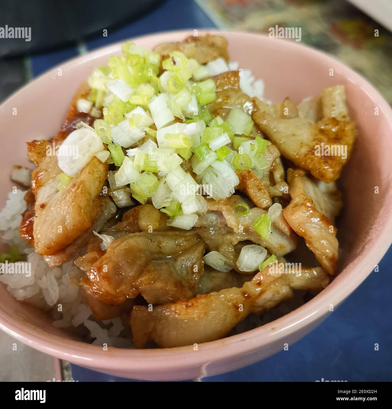 Porc grillé à la sauce soja recouvert de riz et d'oignon de printemps. Aliments faits maison dans une tasse en céramique rose Banque D'Images