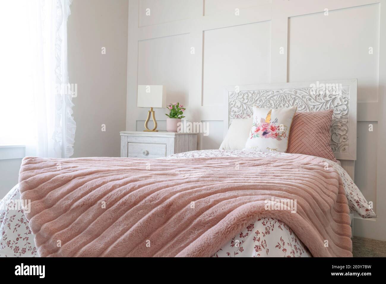 Chambre féminine avec draps fleuris et couverture rose sur le lit contre le mur Banque D'Images