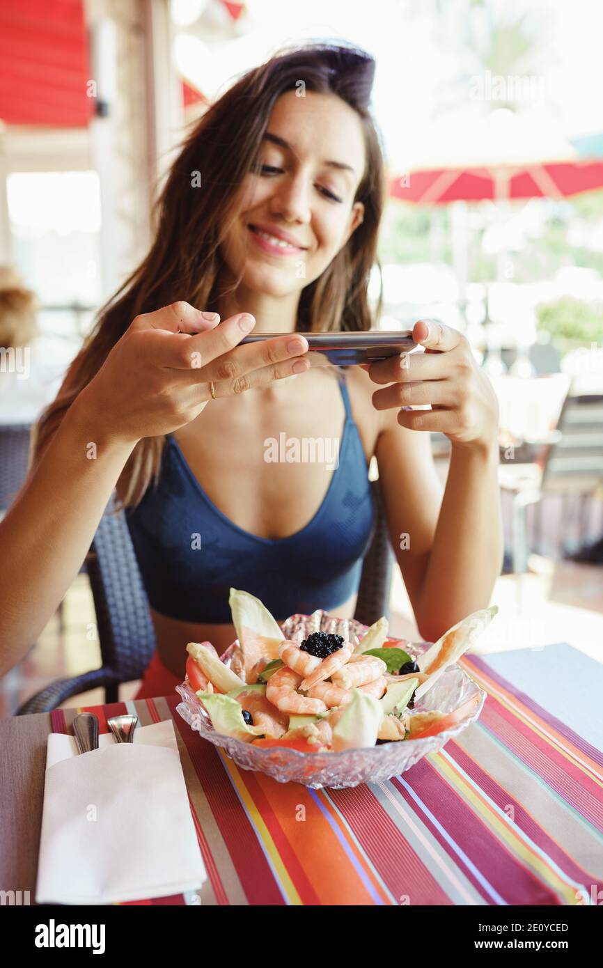 Jeune femme photographiant sa salade avec un smartphone tout en étant assise dans un restaurant Banque D'Images